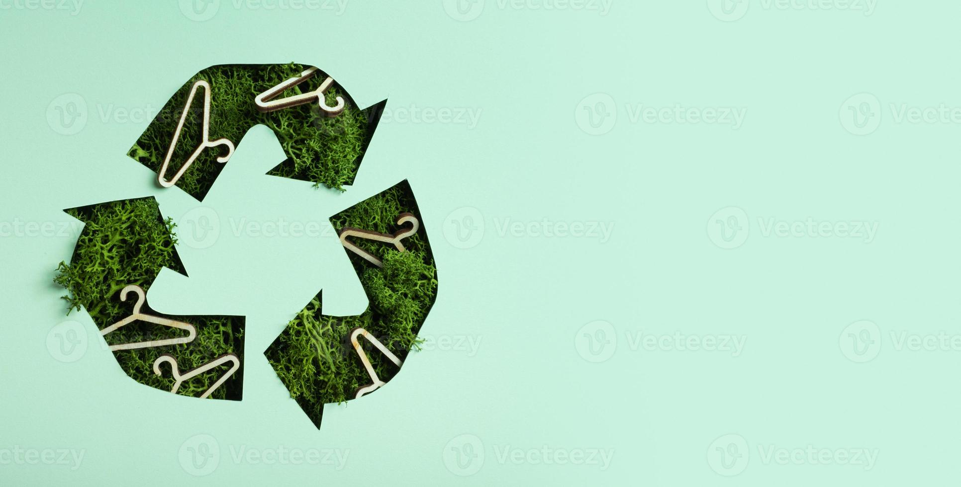 Green moss and hangers under paper cut recycling symbol. Fast fashion, slow fashion, recycling cloth concept photo