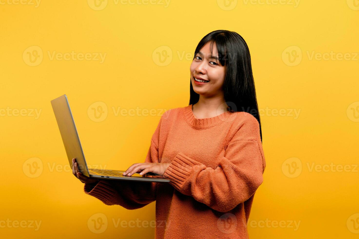 online communication concept asian girl use laptop at home yellow studio photo She is happy to spend her free time online while chatting with friends on social networks, shopping or working online.