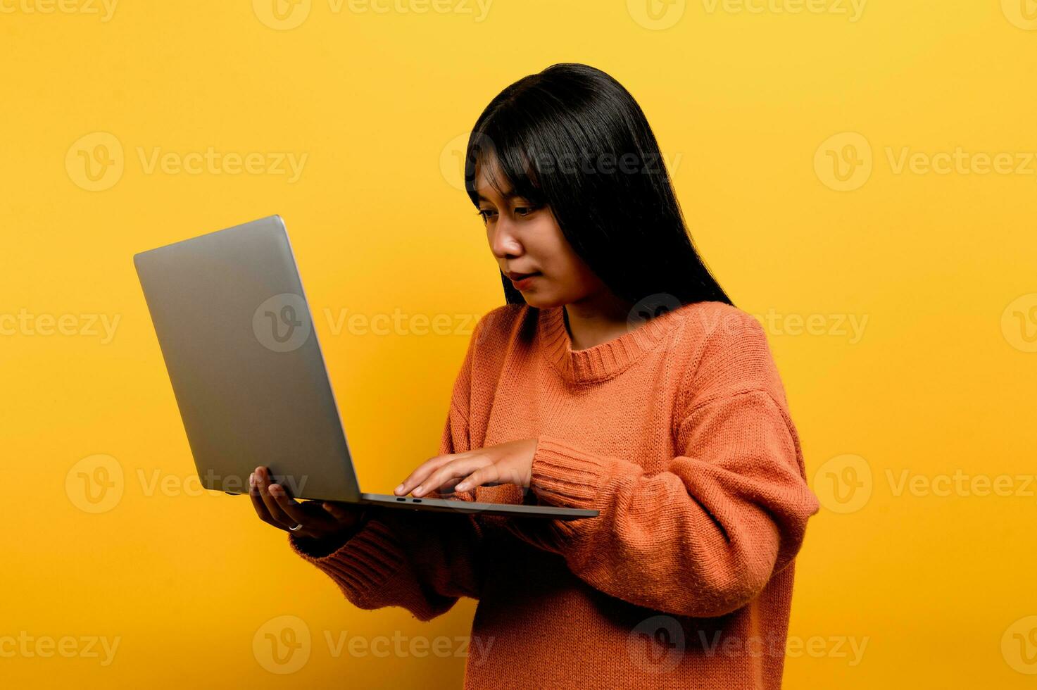 online communication concept asian girl use laptop at home yellow studio photo She is happy to spend her free time online while chatting with friends on social networks, shopping or working online.