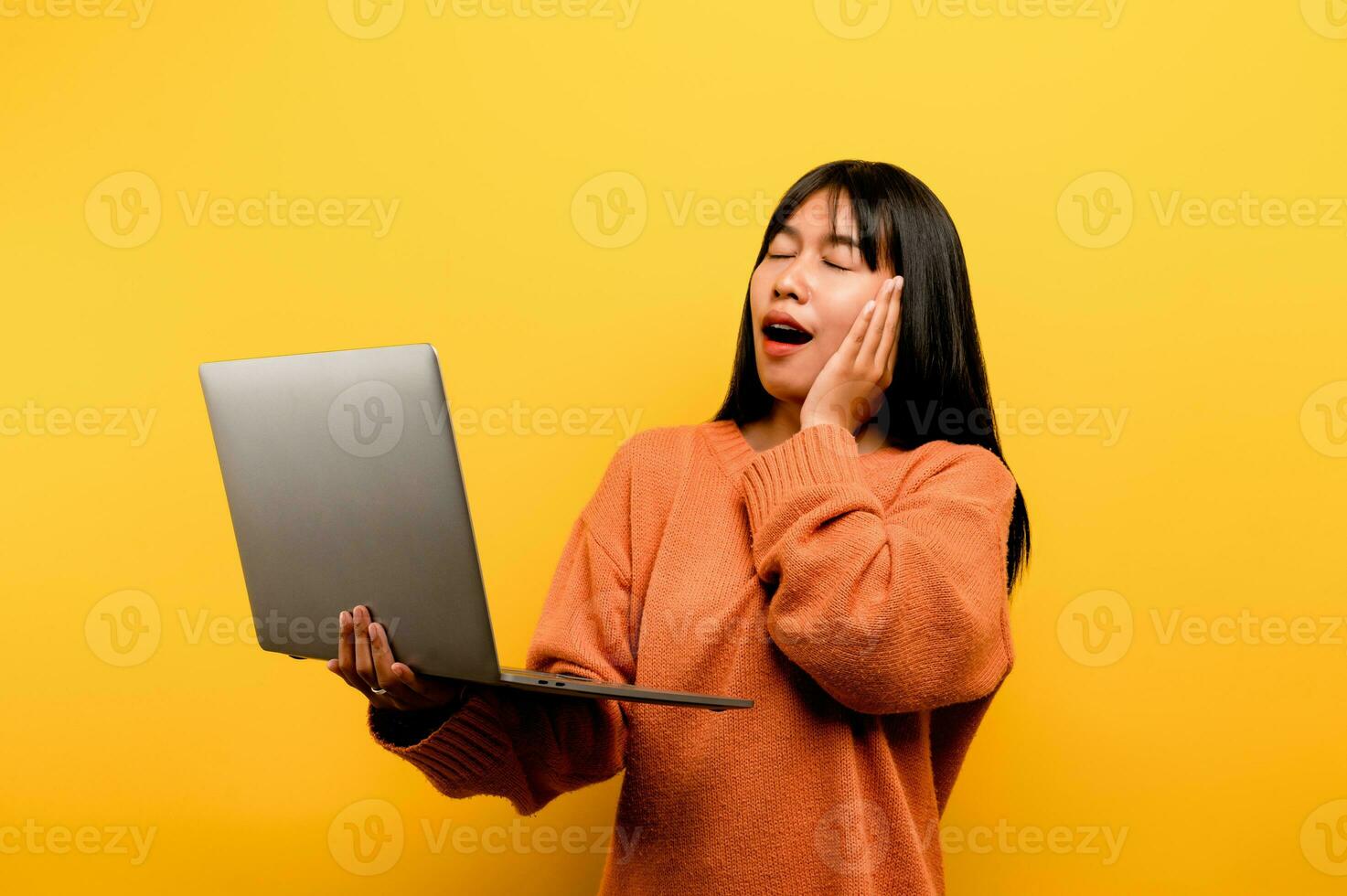 online communication concept asian girl use laptop at home yellow studio photo She is happy to spend her free time online while chatting with friends on social networks, shopping or working online.