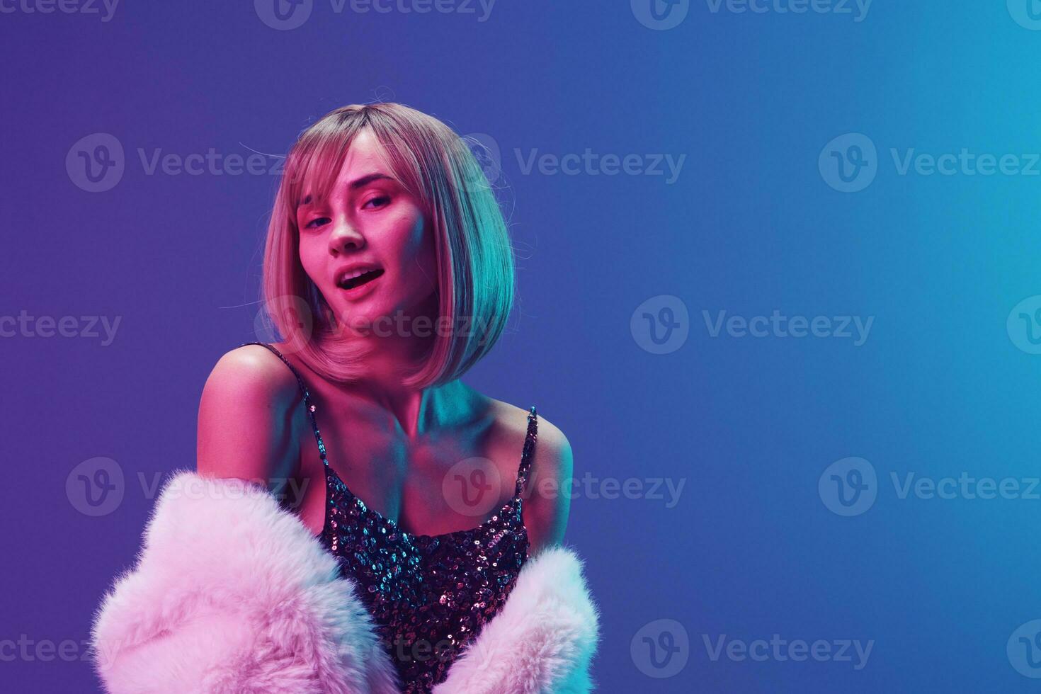 Sexy adorable blonde woman in fluffy fur coat sparkly dress with naked shoulders posing isolated in blue violet pink color light studio background. Neon party Fashion concept. Copy space Banner photo
