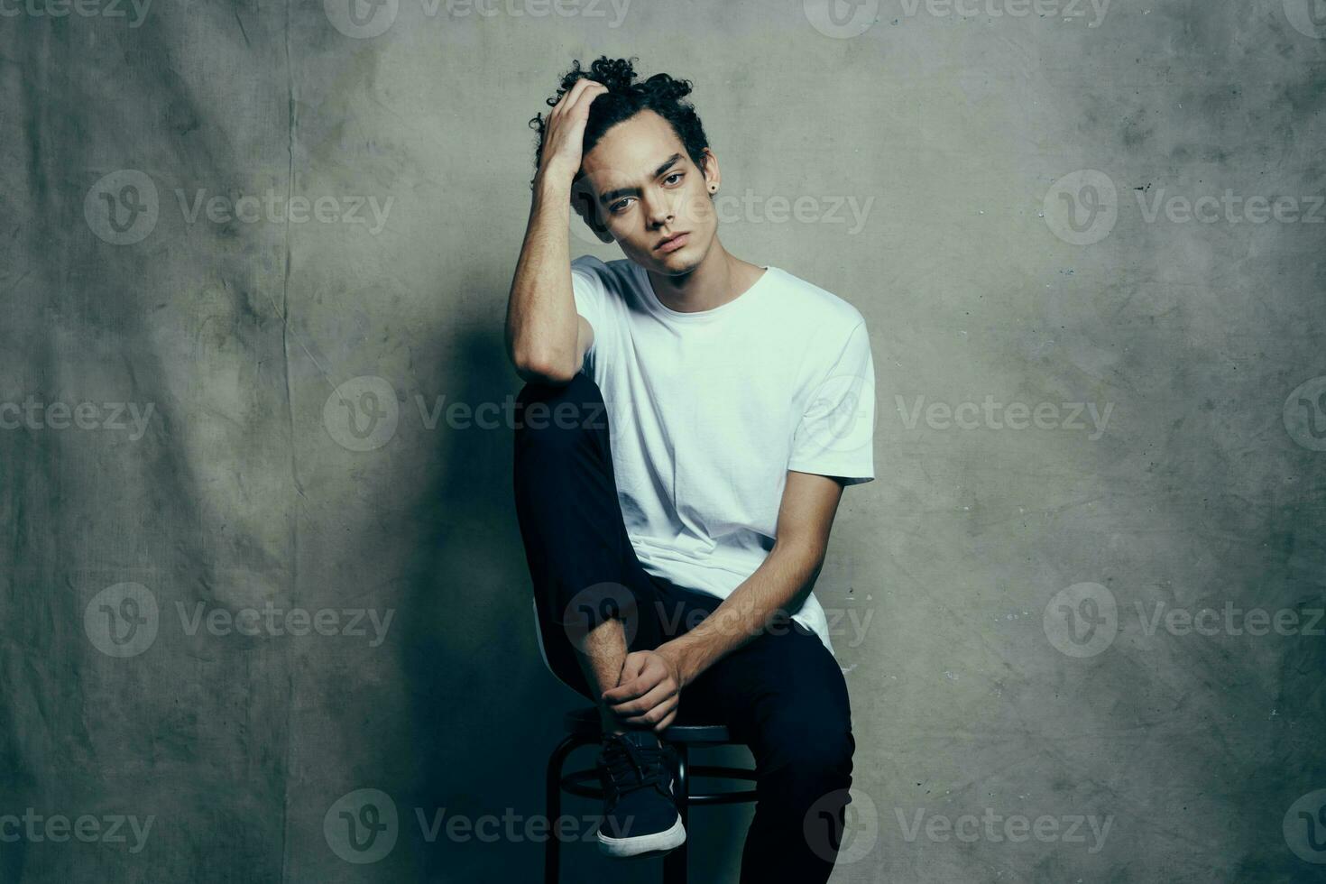 hombre con Rizado pelo sentado en un silla Moda estudio foto