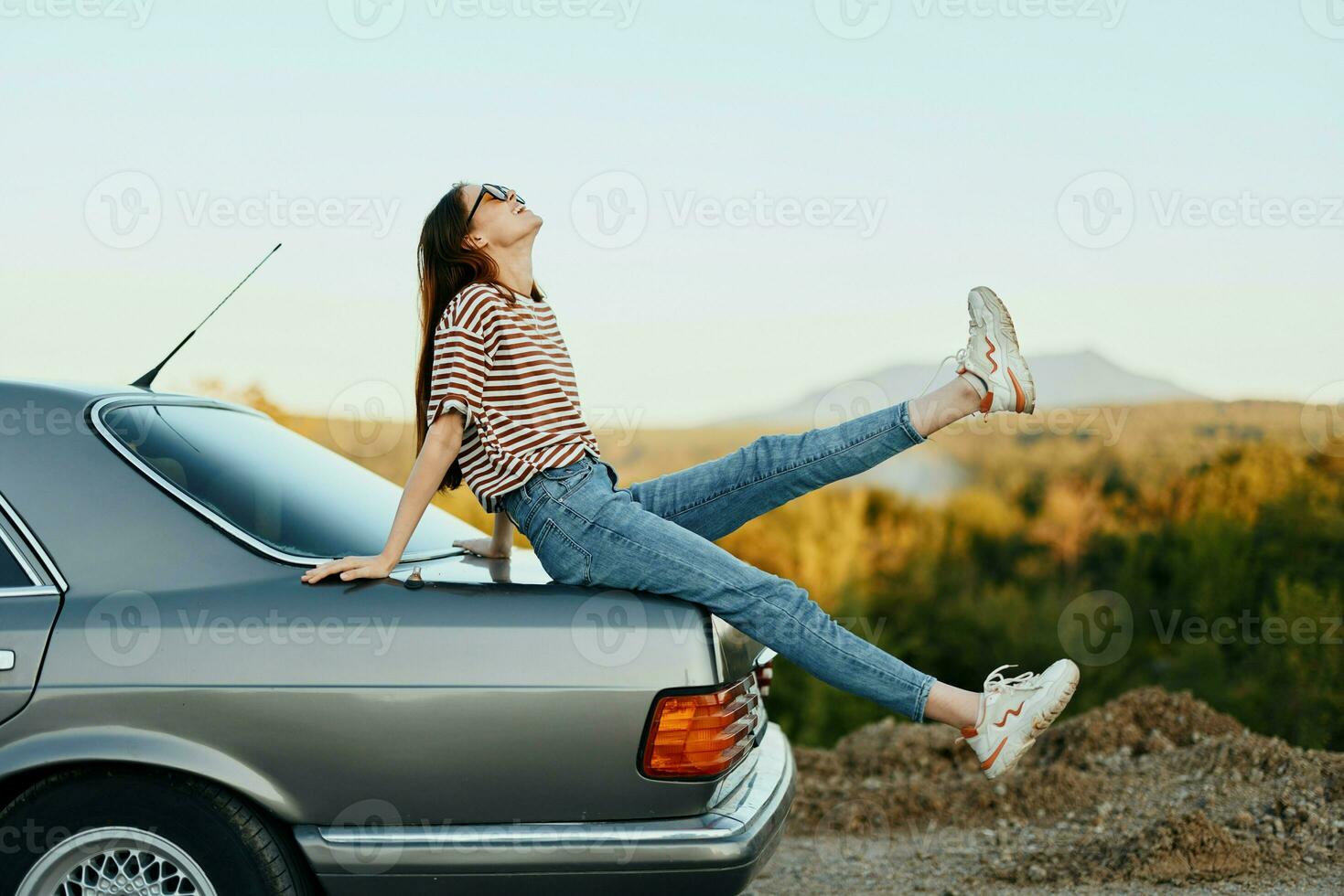 A woman with a car stopped on the road to rest on the journey raised her arms and legs from happiness and a beautiful landscape photo