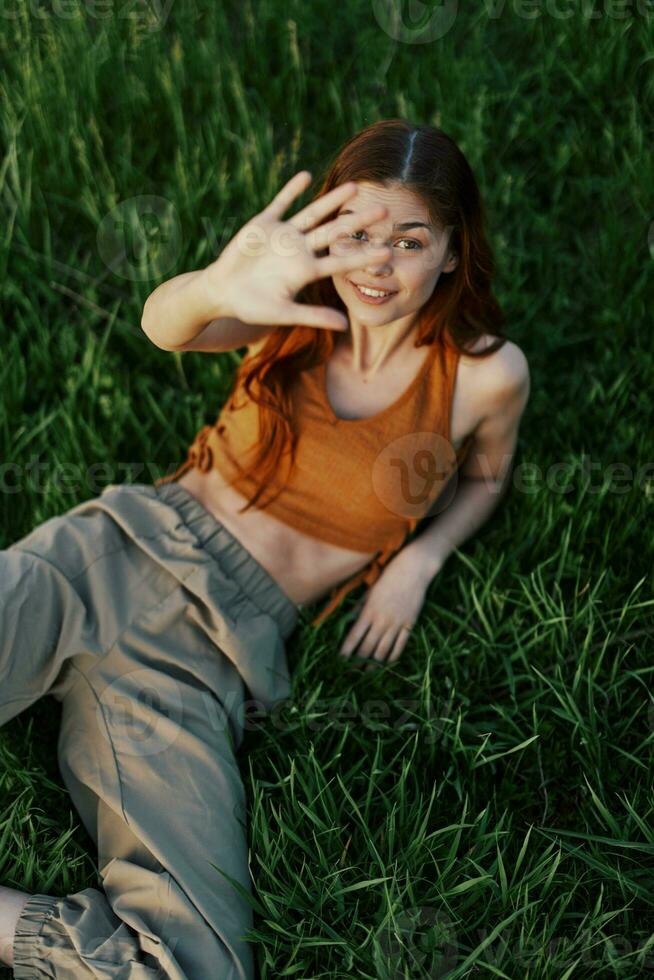 The view from above is a woman lying on the green grass in the park and relaxing in nature smiling and enjoying life. The concept of a healthy lifestyle photo