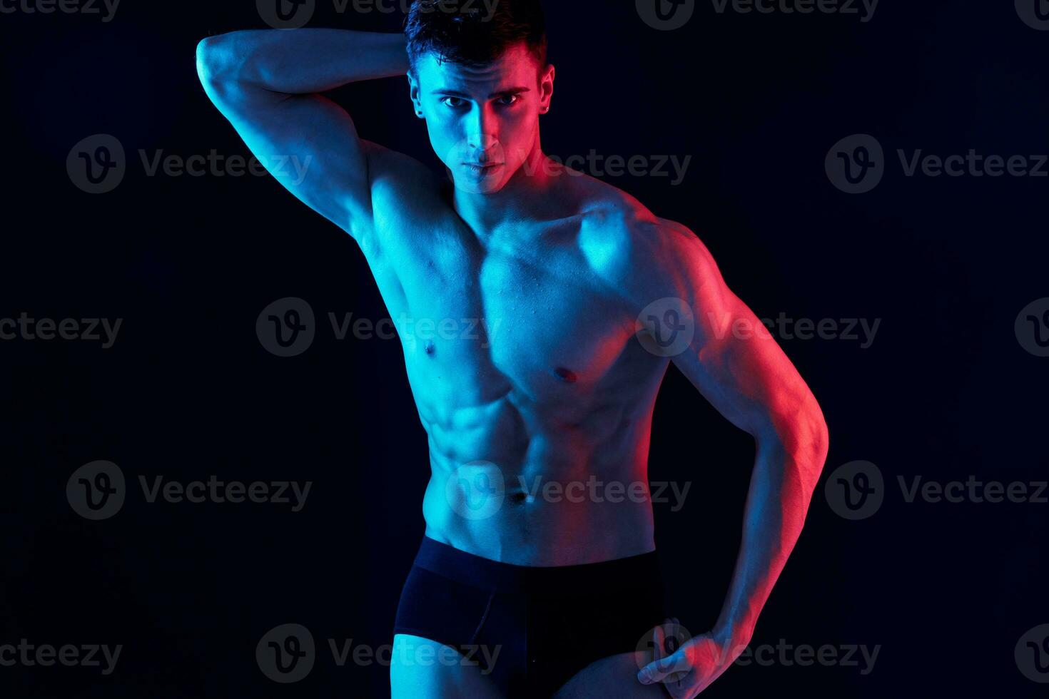 guy athlete with a pumped-up torso holds his hand above his head on a black background photo