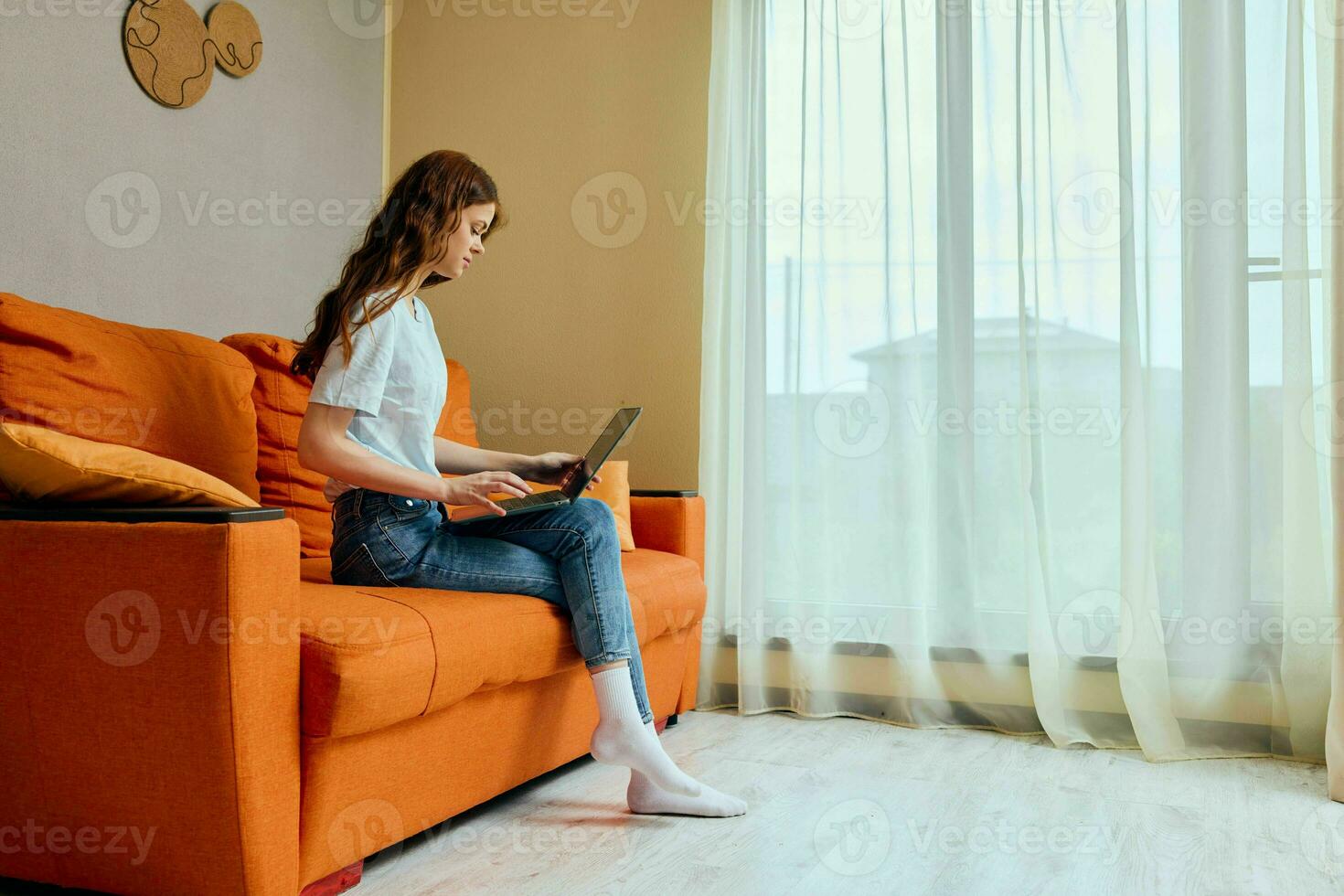 pretty woman chatting on the orange couch with a laptop apartments photo