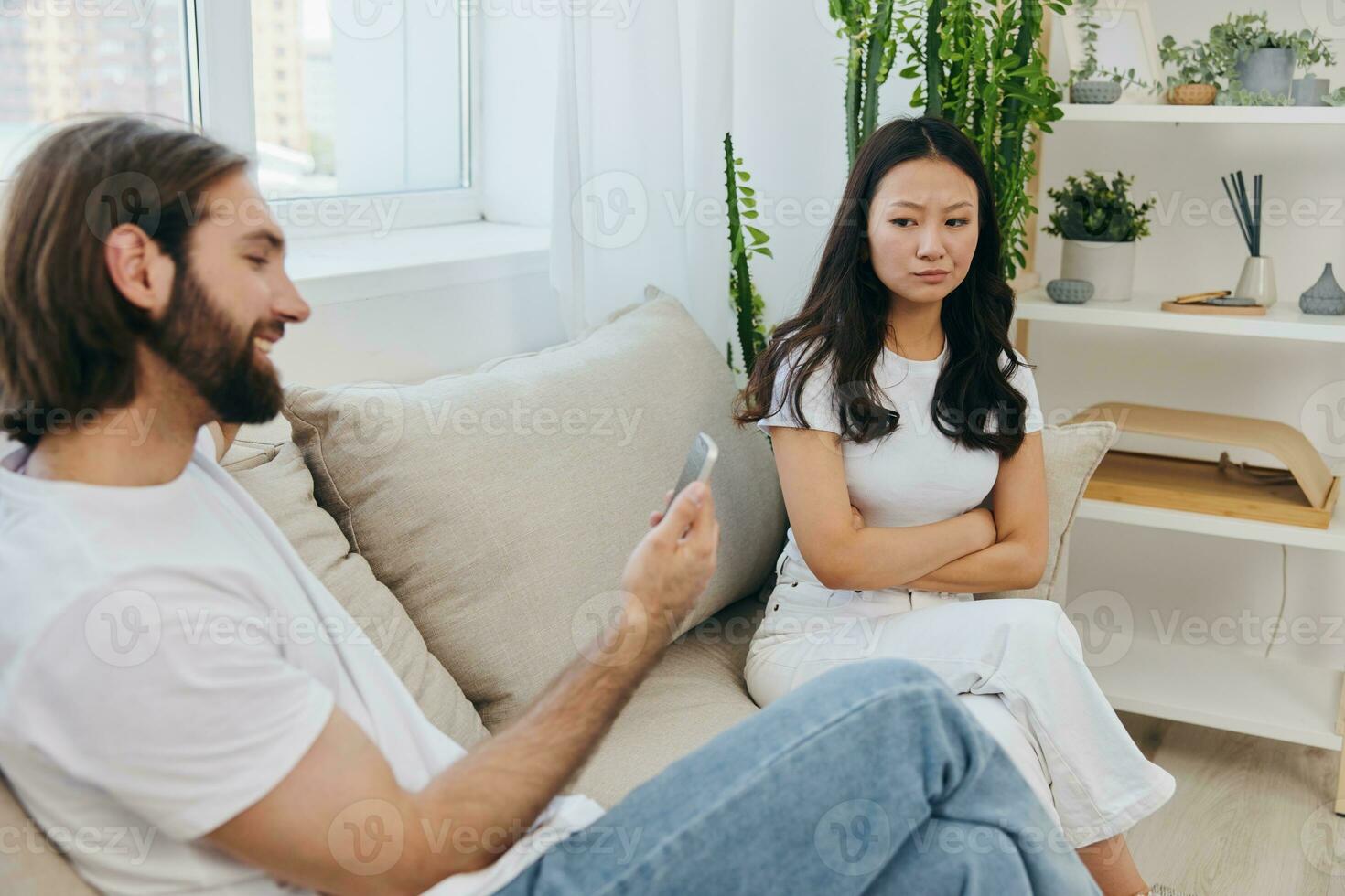 A man looks at the phone screen during an argument with his girlfriend. The angry and hurt woman looks in his direction and is sad. Family discord at home, phone addiction photo