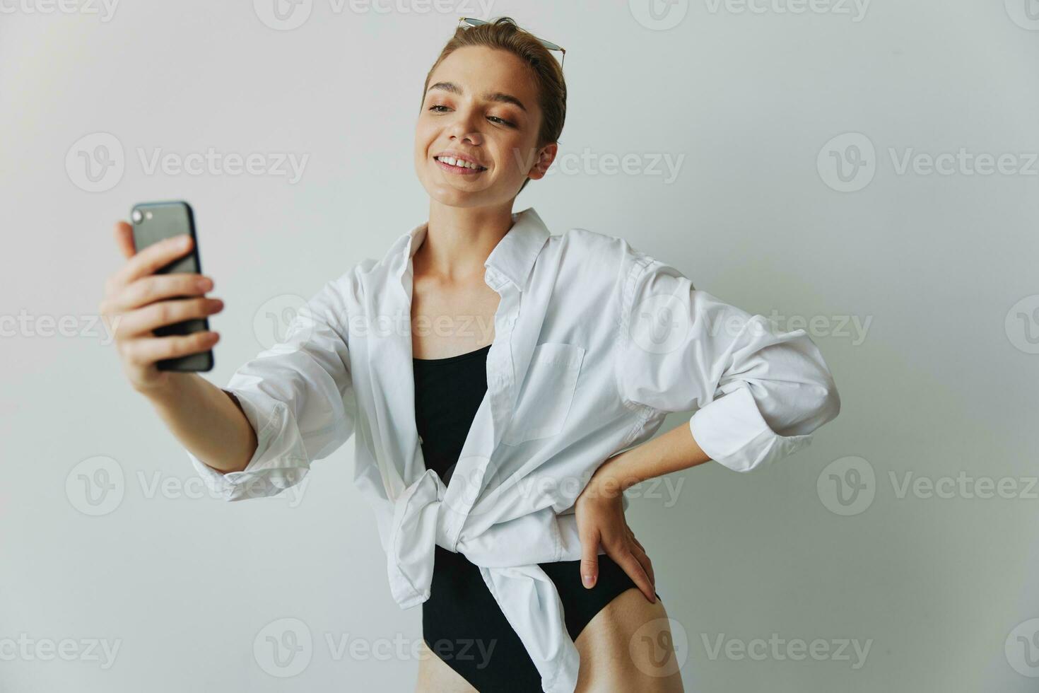 Teenage girl blogger takes photos and shoots. herself on video on her phone for social media content, video blogger, selfies against a white wall with a smile at home, freelancer