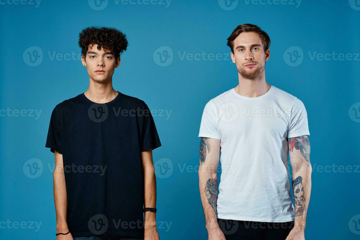 two men in t-shirts on a blue background stand side by side cropped view portrait photo