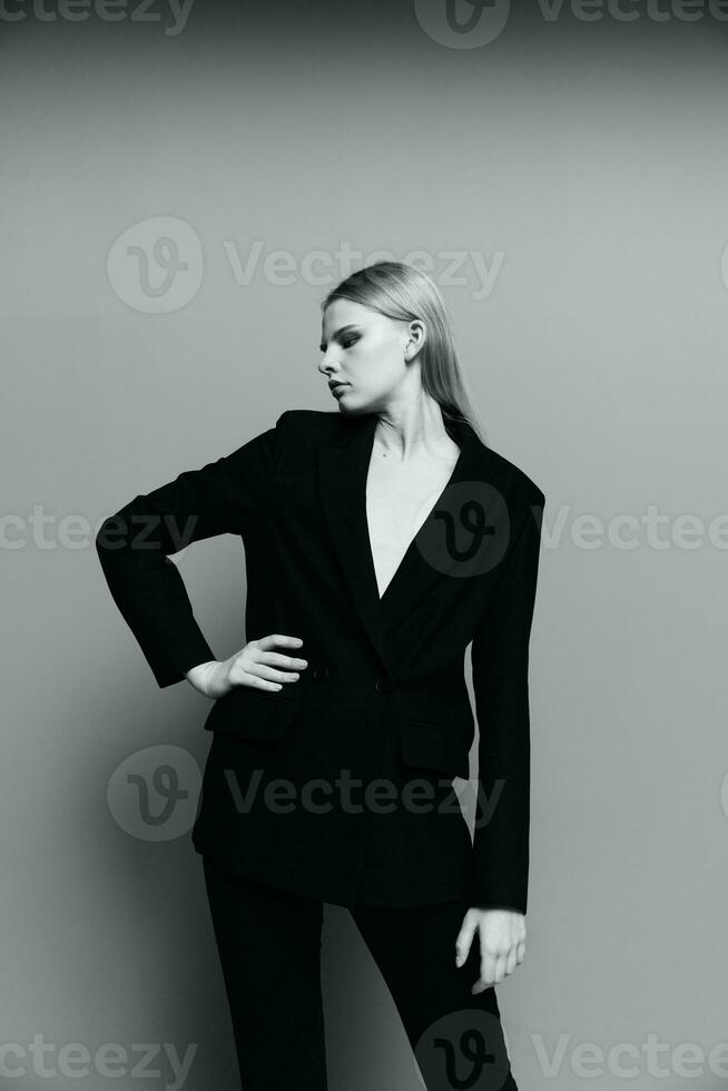 A stylish lady in a suit keeps her hand on her waist and looks away photo