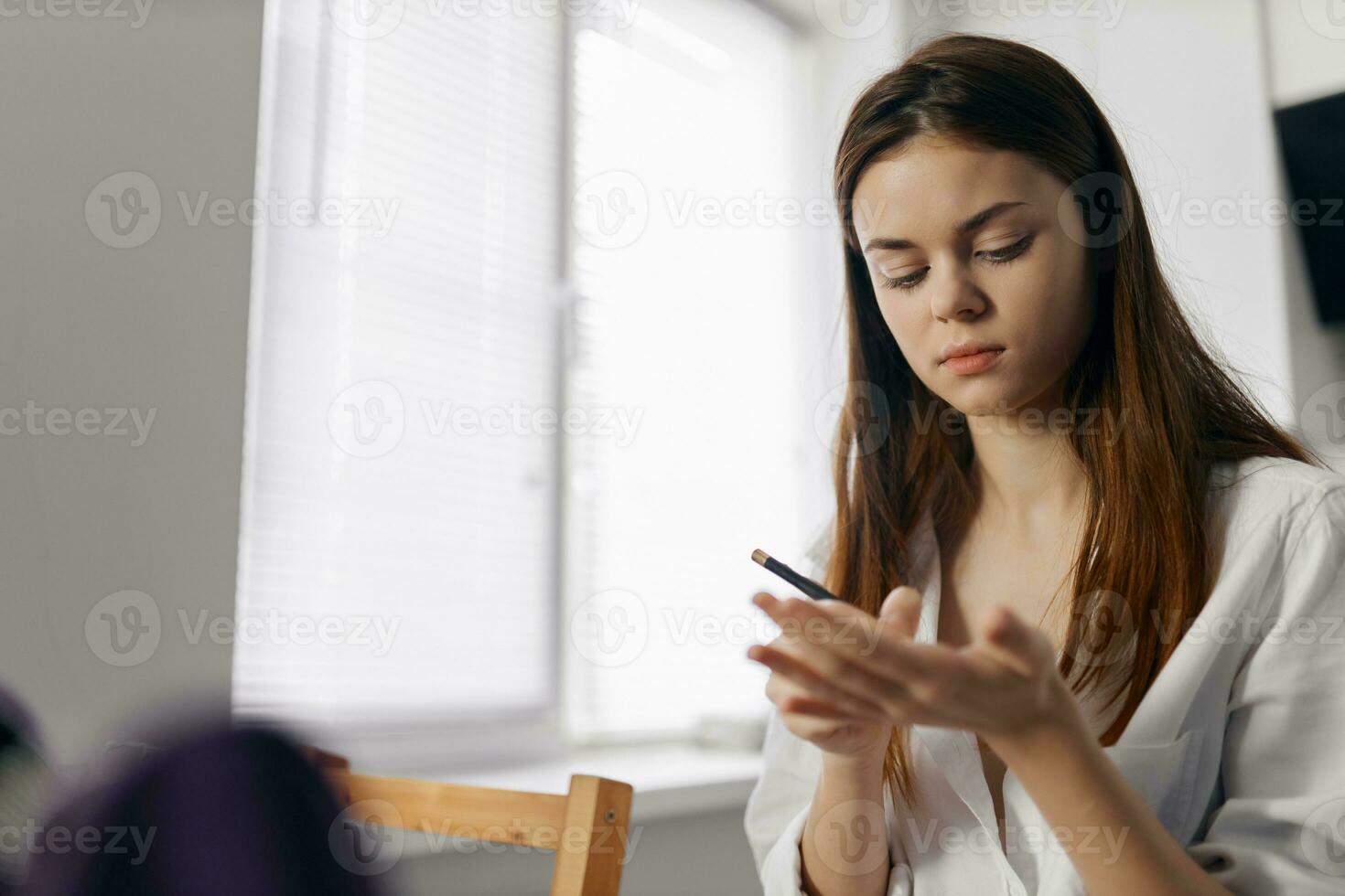 woman holding makeup pencil in hand indoors near window photo