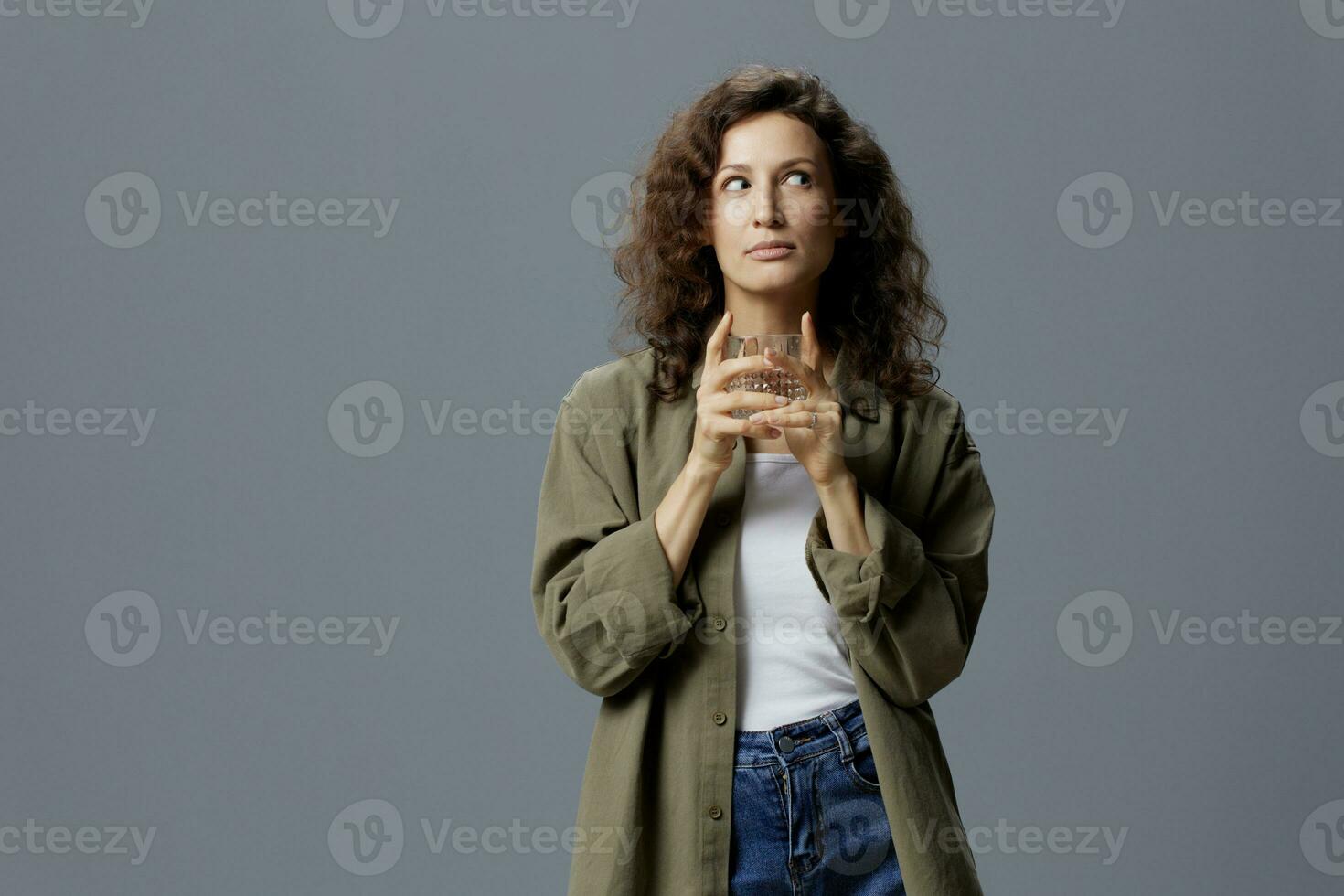 soñando Rizado hermosa mujer en casual caqui verde camisa sostener vaso de agua pensando mira aparte posando aislado en terminado gris azul antecedentes. sano estilo de vida. agua es vida concepto. Copiar espacio foto