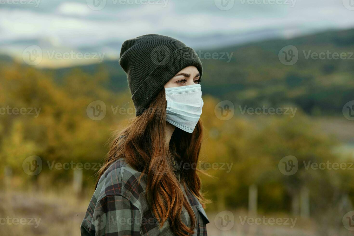 Traveler with a medical mask on her face and a hat in the autumn forest photo