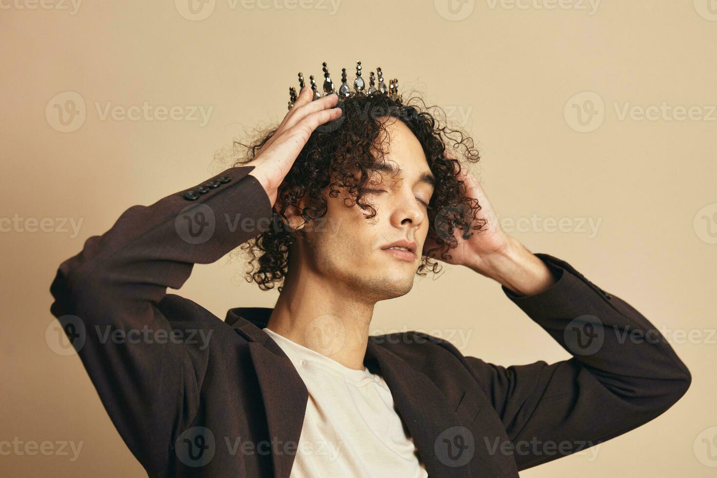 Pretty cute handsome funny narcissistic tanned curly man with crown posing isolated on over beige pastel background. Fashion New Collection offer. Retro style concept. Free place for ad photo