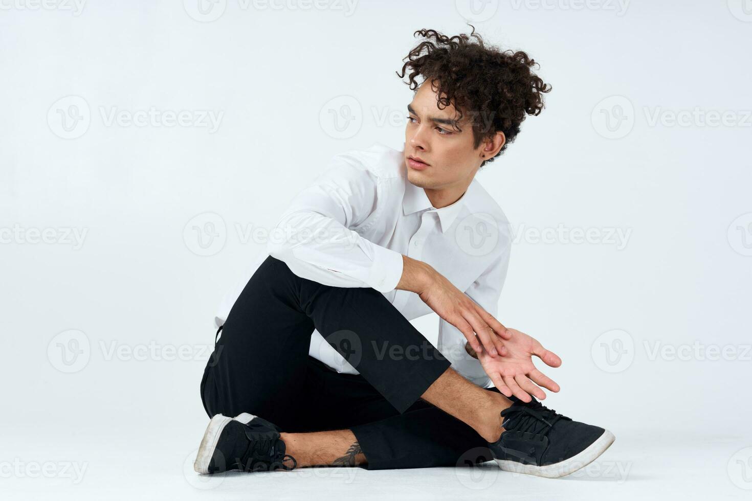 young man with curly hair sits cross-legged on the floor photo