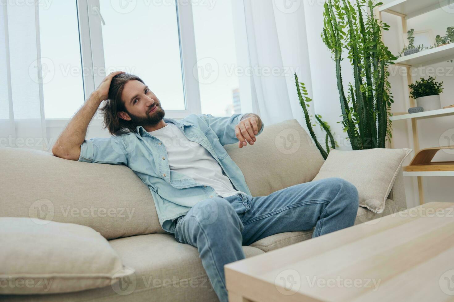 A young male freelancer sits on the couch after a demanding job and rests sadly leaning on the couch. photo