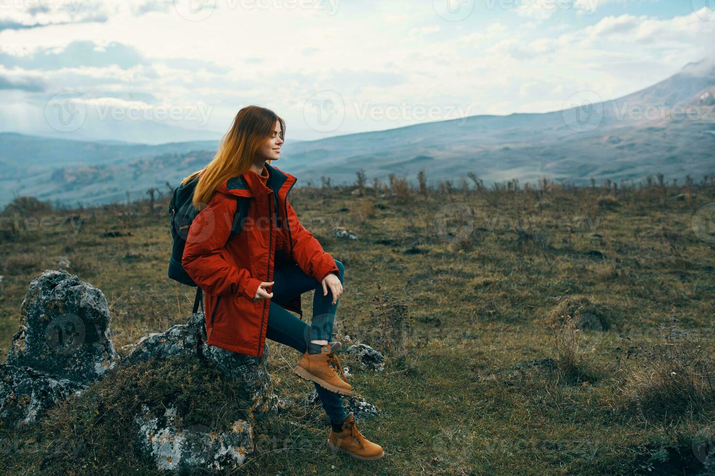 woman traveler in a jacket sits on the Big Stone and looks at the mountains landscape photo