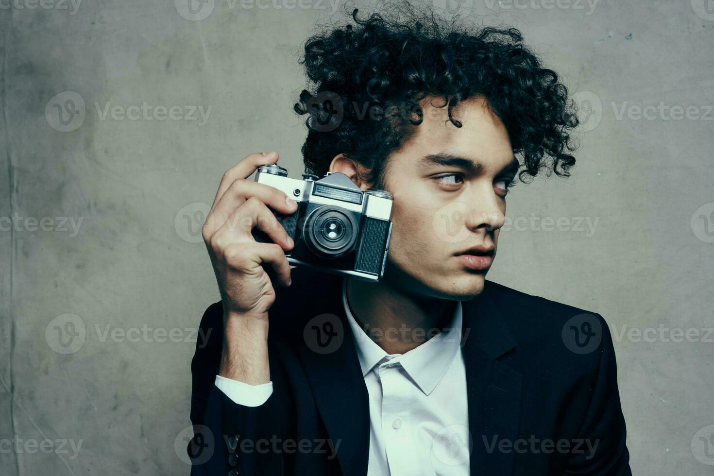 curly-haired man in a jacket and shirt holding a camera in his hand model vogue style photo