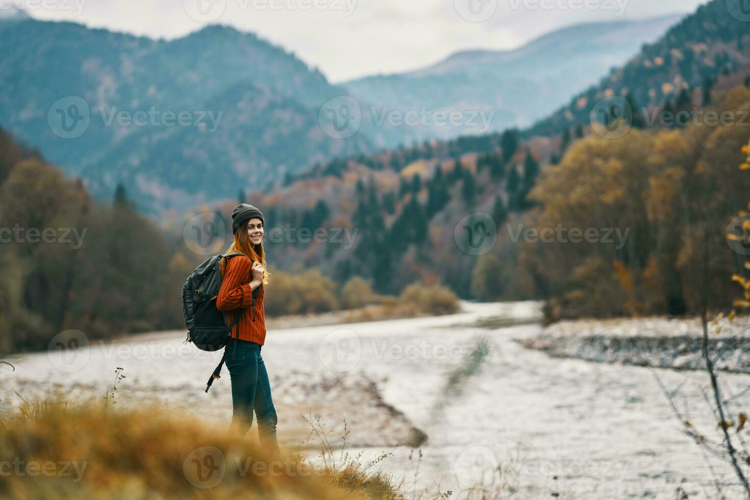 young traveler with a backpack in jeans and a sweater near the river in the mountains photo