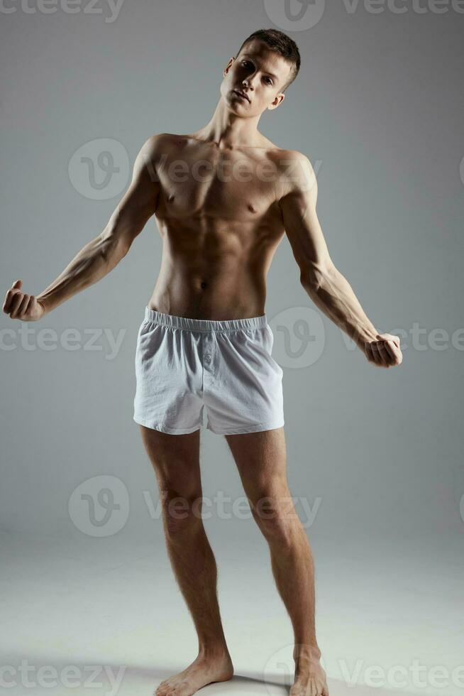 male bodybuilder in shorts gesturing with his hands on a gray background full growth photo