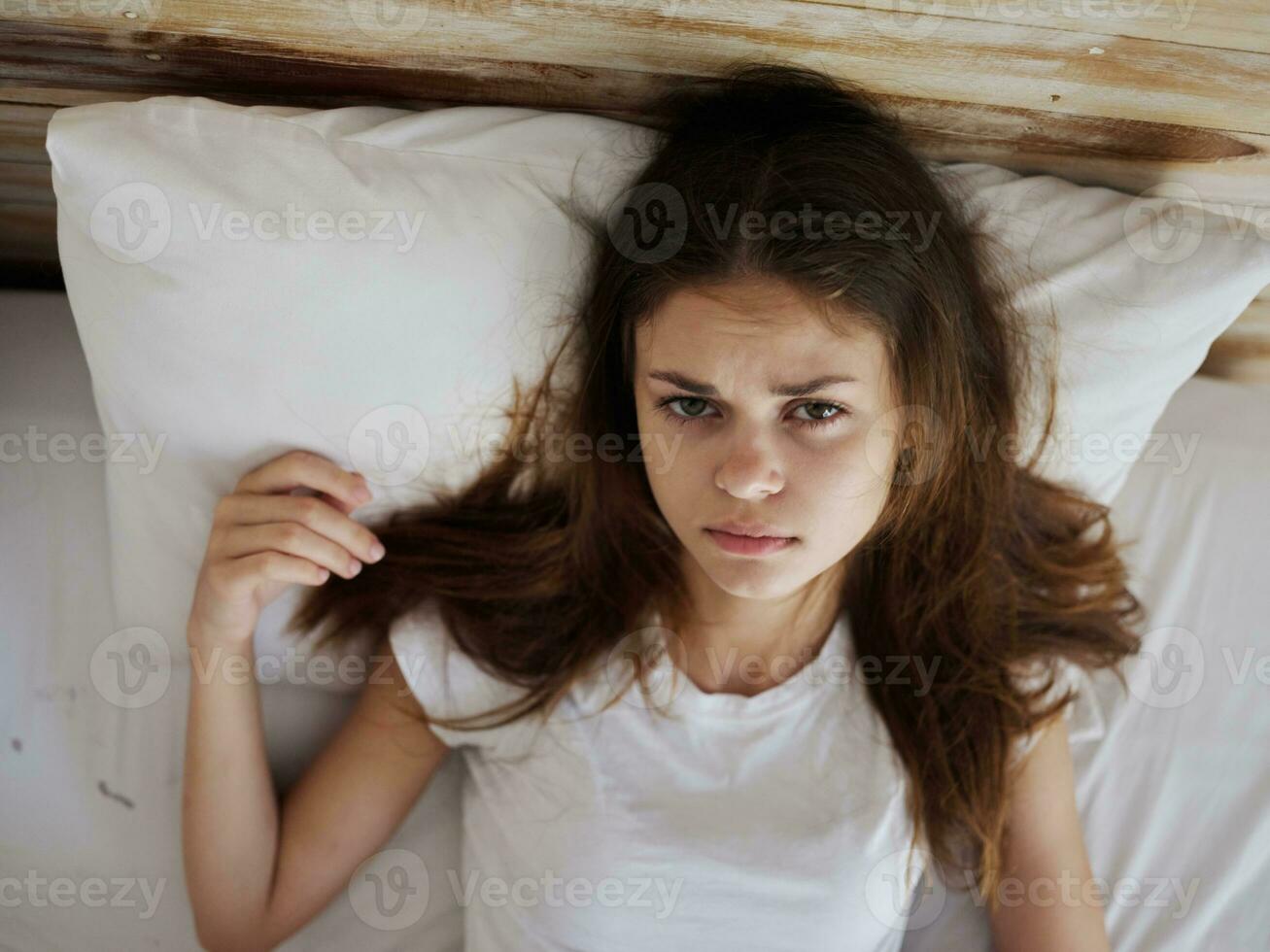 un mujer mentiras en cama en un blanco camiseta sensación indispuesto de cerca foto