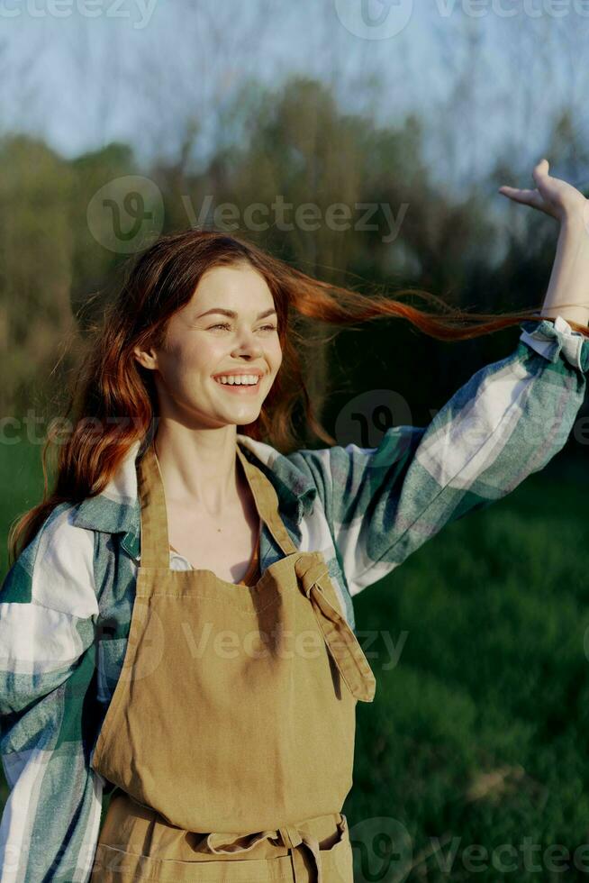 Portrait of a beautiful young woman with red hair in nature in a park in the summer, looking at the sunset against a background of green grass and trees photo