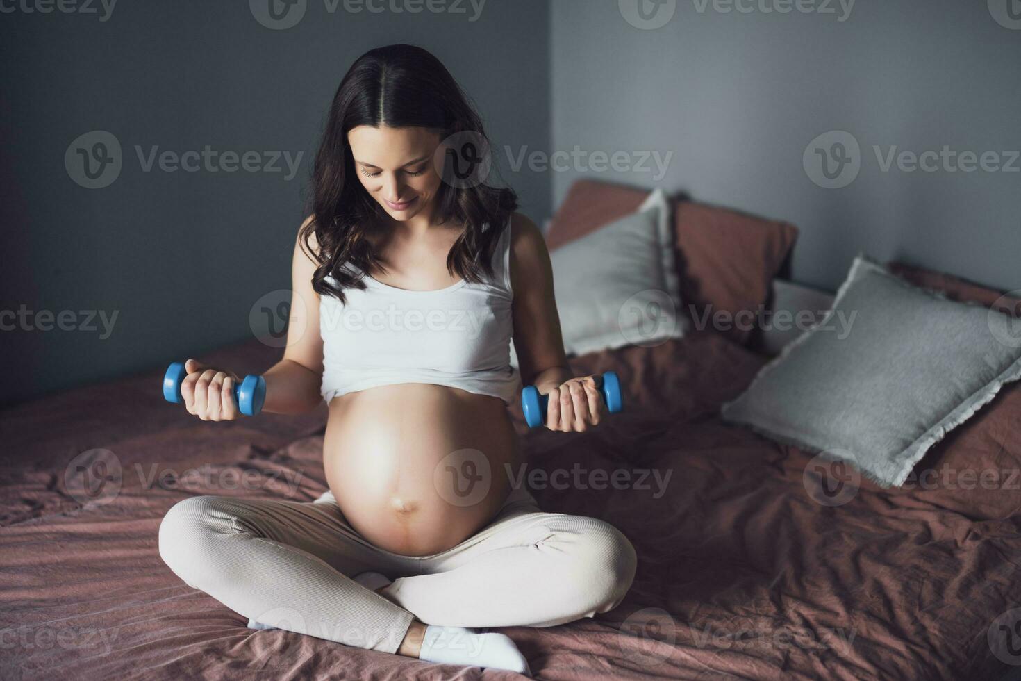 Pregnant woman is exercising with weights at home. photo