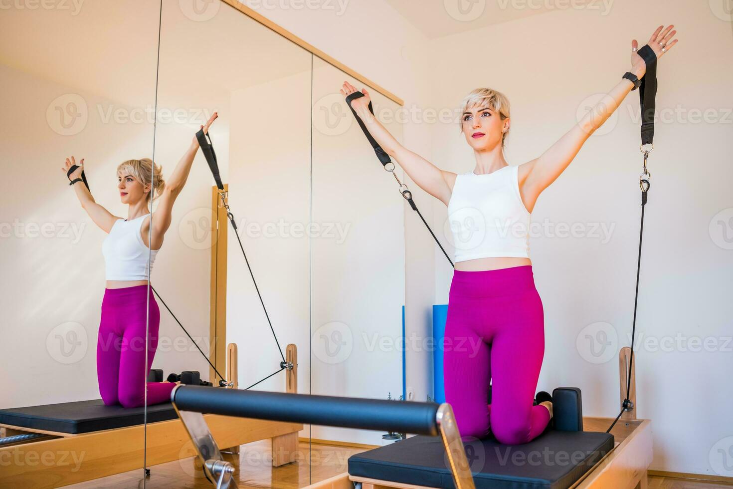 Blonde woman is exercising on pilates reformer bed in her home. photo