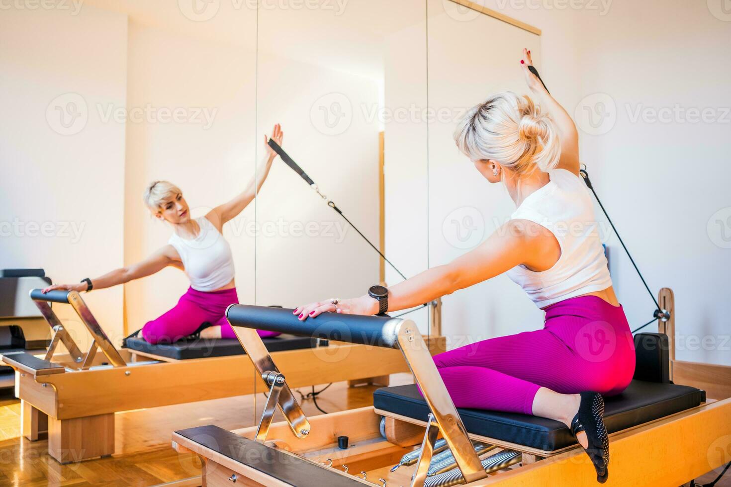 Blonde woman is exercising on pilates reformer bed in her home. photo