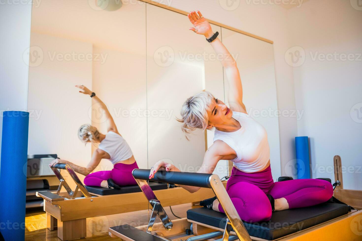 Blonde woman is exercising on pilates reformer bed in her home. photo