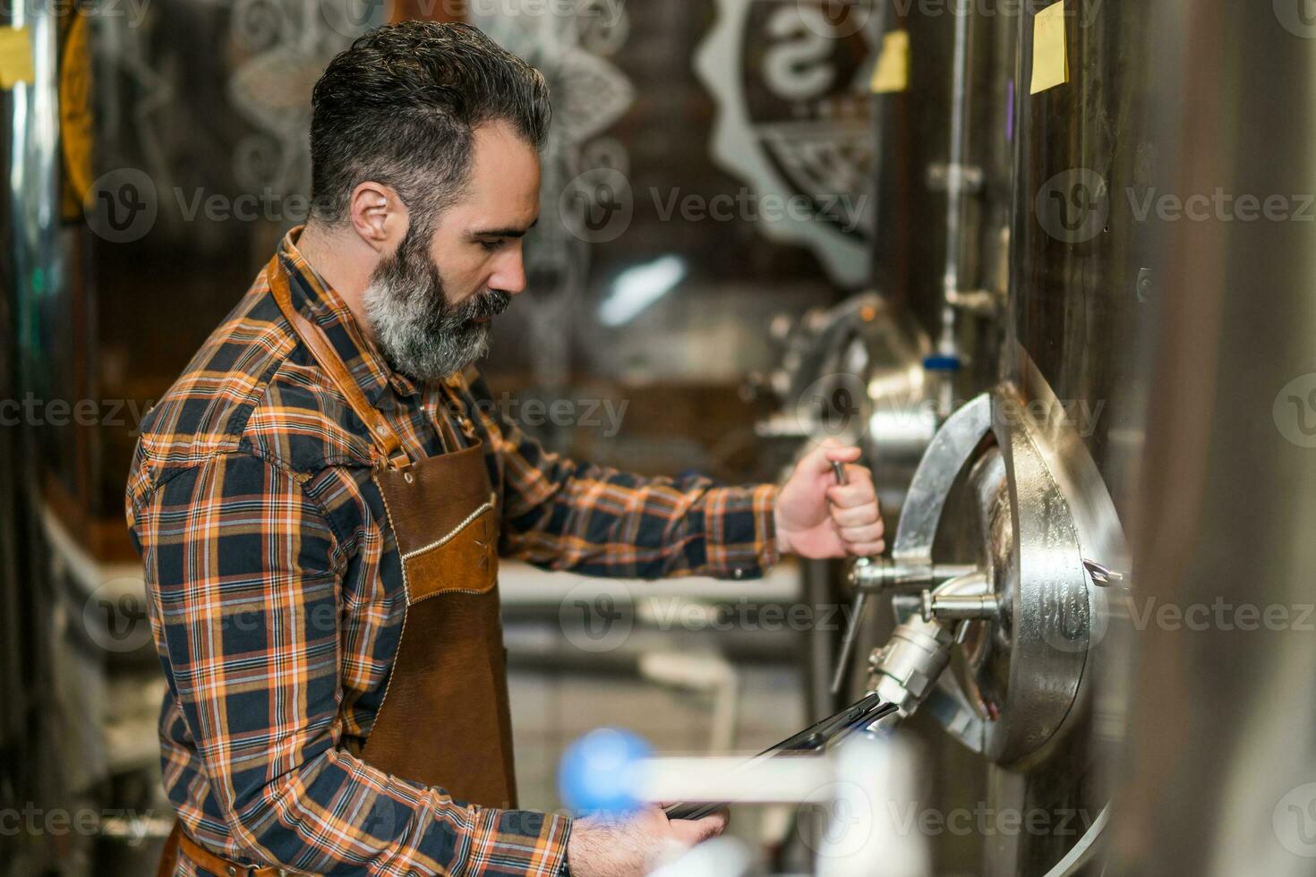 Man is working at craft beer factory. He is operating machinery in brewery. Small family business, production of craft beer. photo