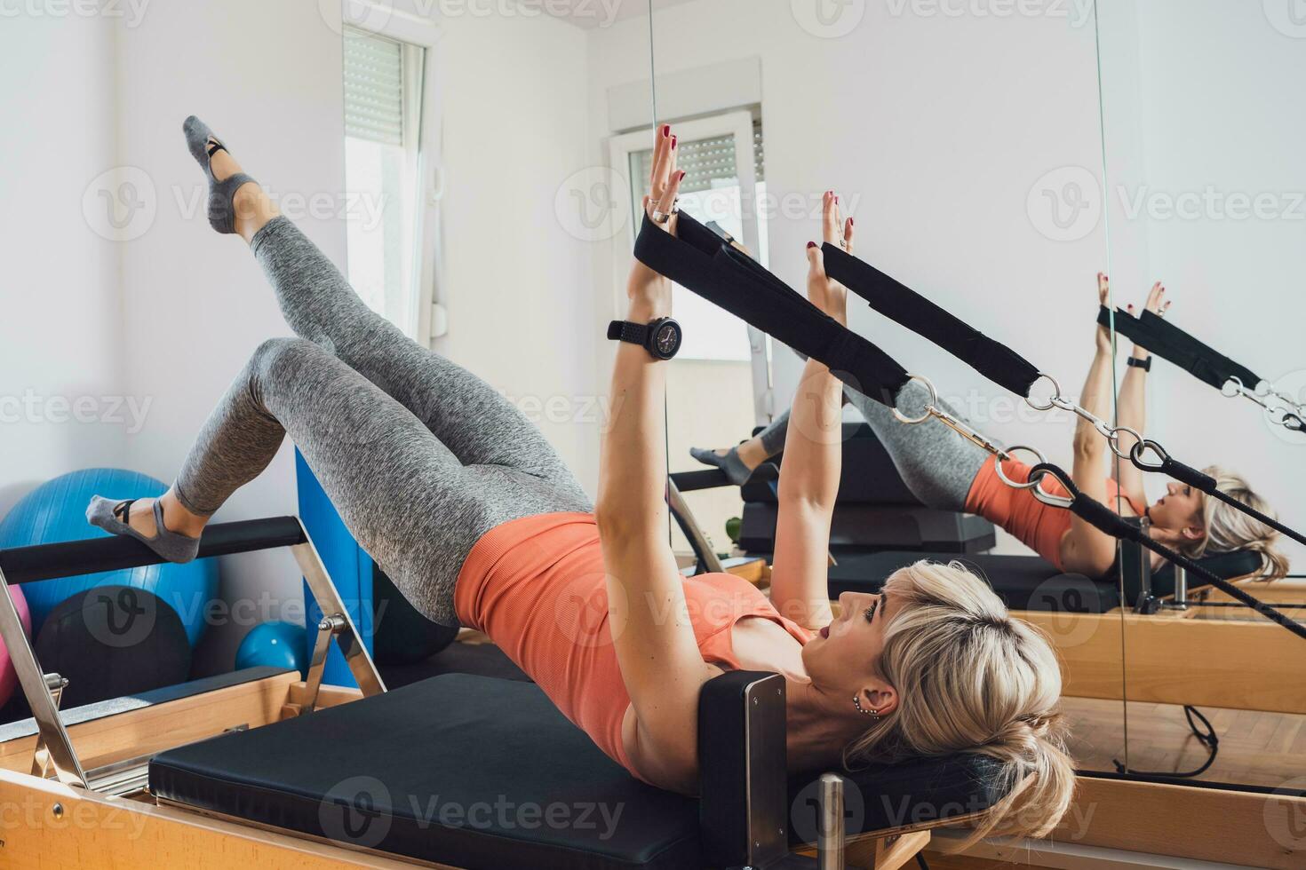 Blonde woman is exercising on pilates reformer bed in her home. photo