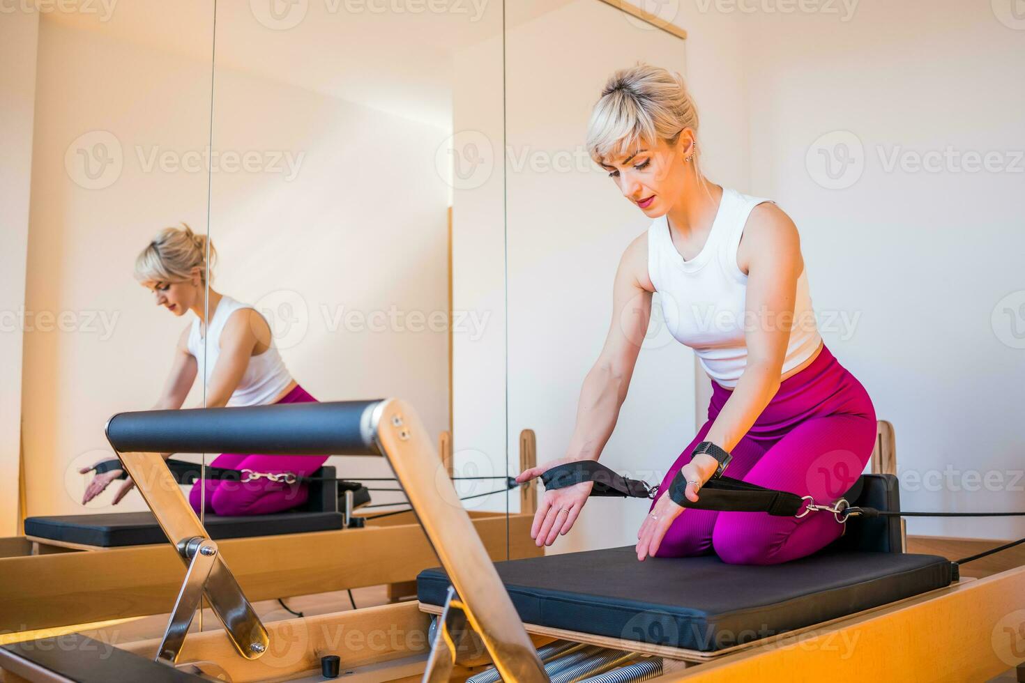 Blonde woman is exercising on pilates reformer bed in her home. photo