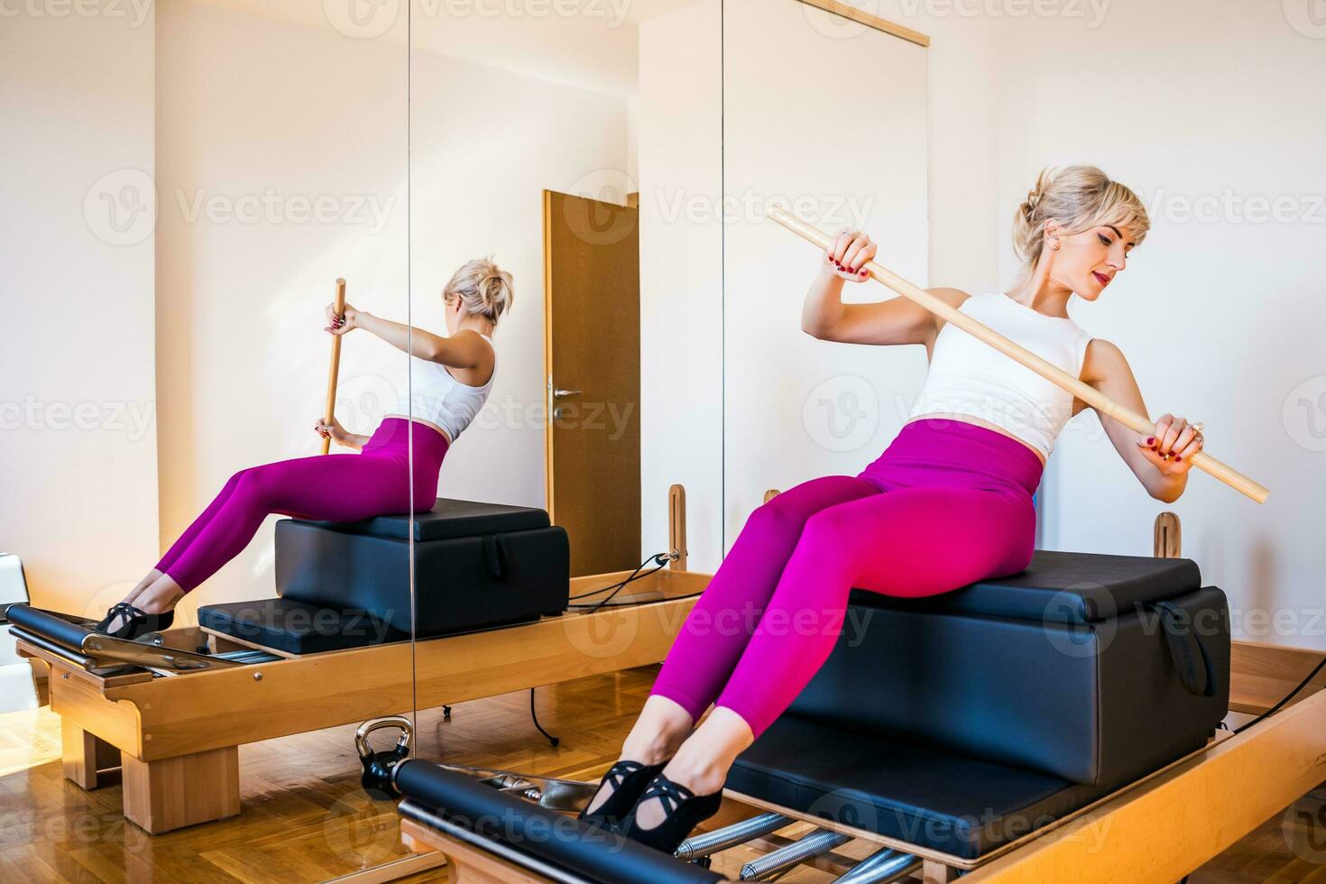 Blonde woman is exercising on pilates reformer bed in her home. photo
