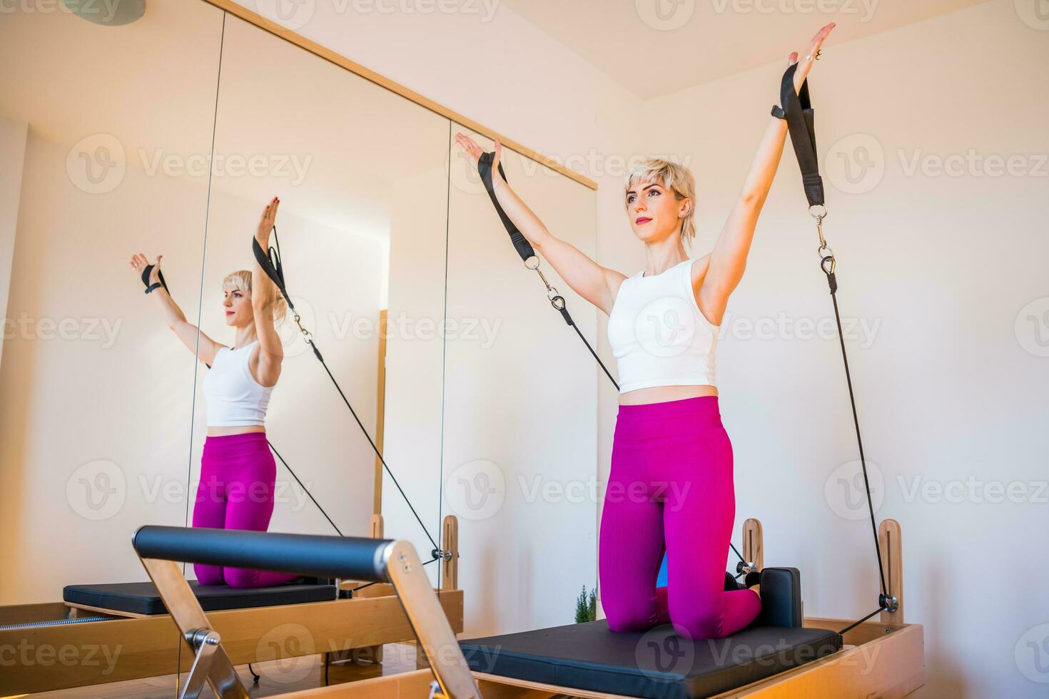 Blonde woman is exercising on pilates reformer bed in her home. photo