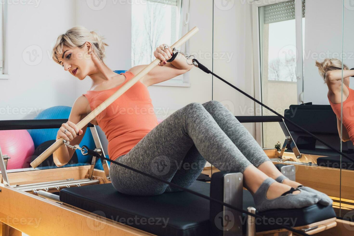 Blonde woman is exercising on pilates reformer bed in her home. photo