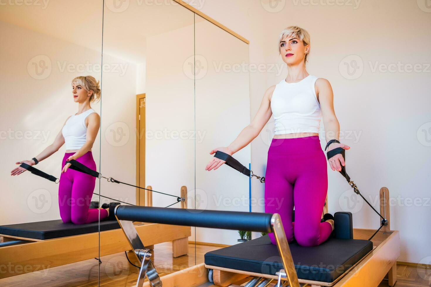 Blonde woman is exercising on pilates reformer bed in her home. photo