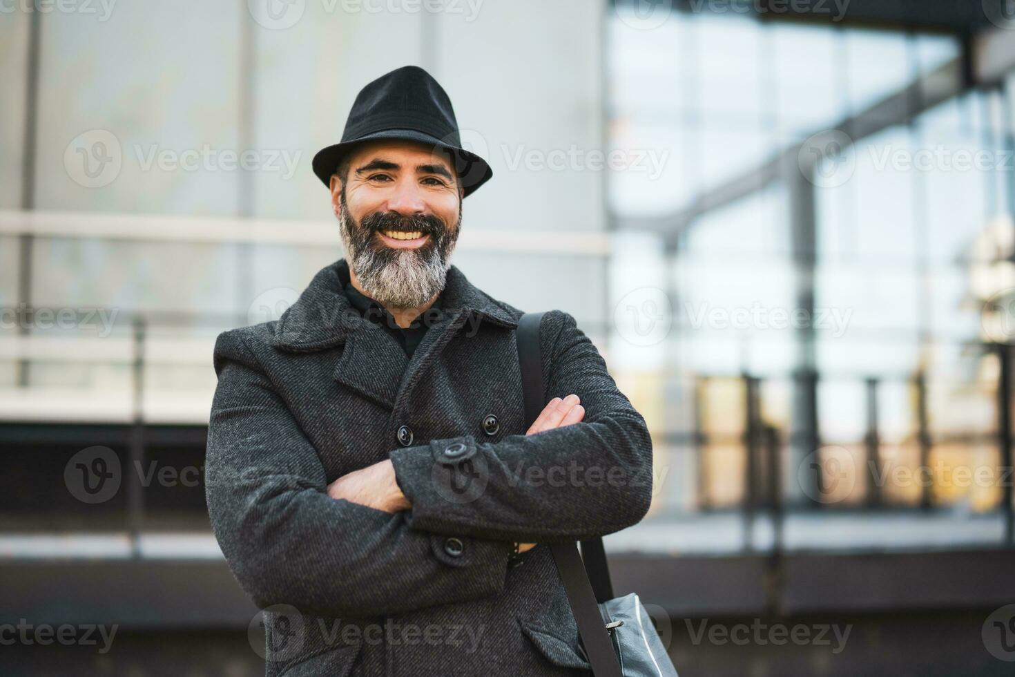 Portrait of happy businessman in black clothing standing in front of company building. Black bearded man is wearing winter clothing and smiling. photo