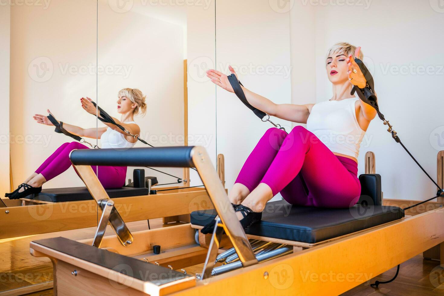 Blonde woman is exercising on pilates reformer bed in her home. photo