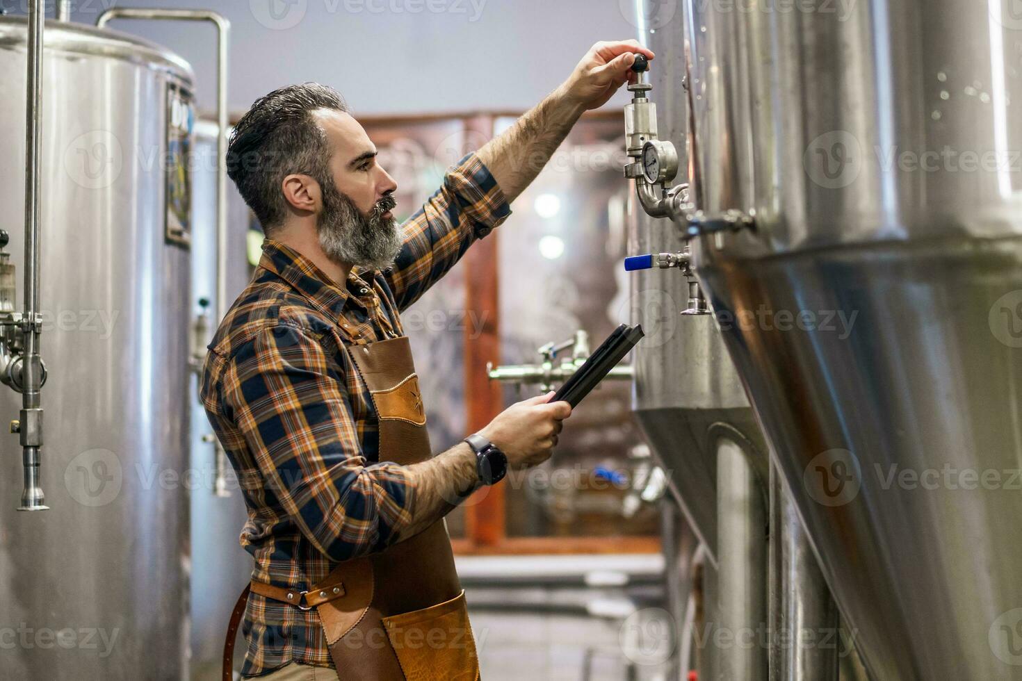 Man is working at craft beer factory. He is operating machinery in brewery. Small family business, production of craft beer. photo