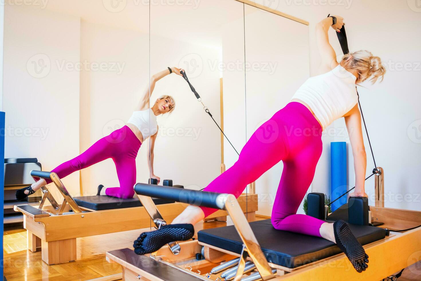 Blonde woman is exercising on pilates reformer bed in her home. photo