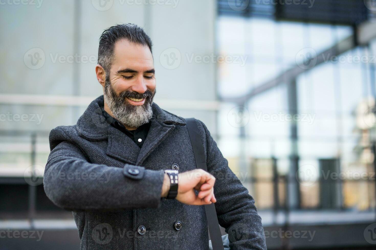 Businessman looking ah his watch in black clothing standing in front of company building photo