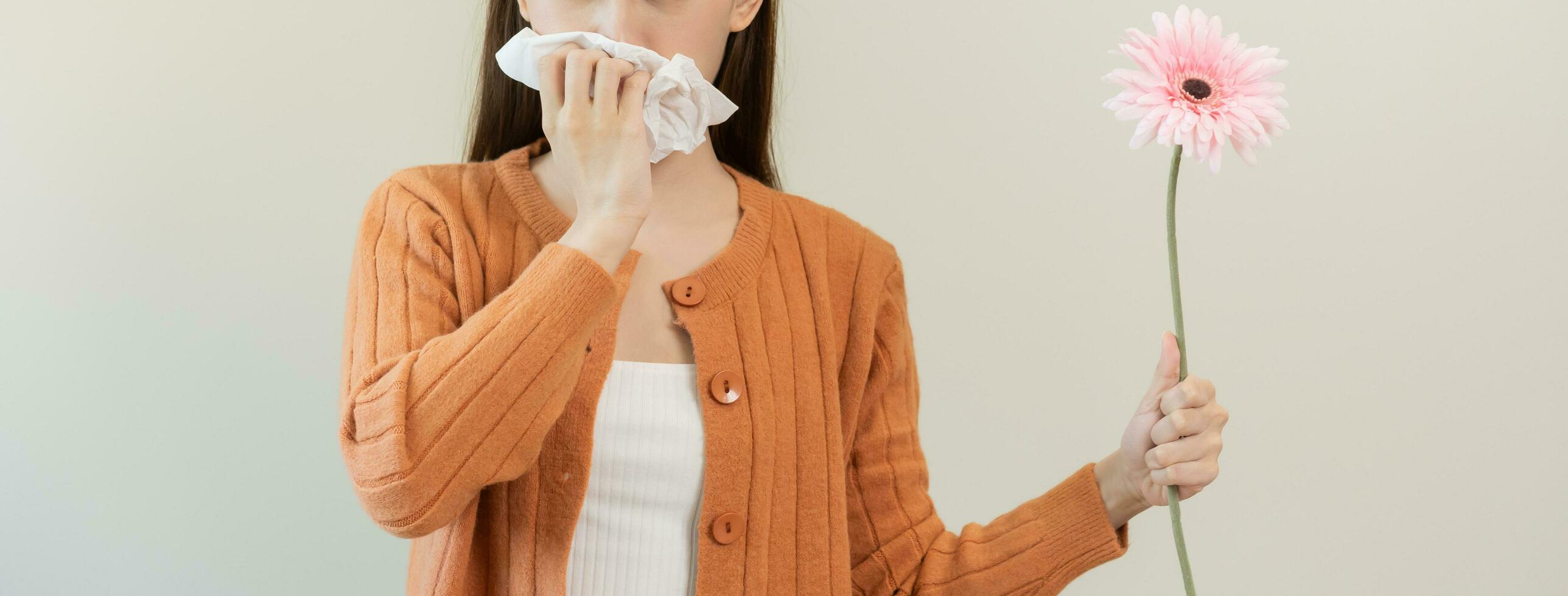 Allergic rhinitis symptom of odor pollen flowering, portrait asian young woman hand in sneeze, blowing runny nose after smell, smelly from bloom flower, holding away pink flora on white background. photo