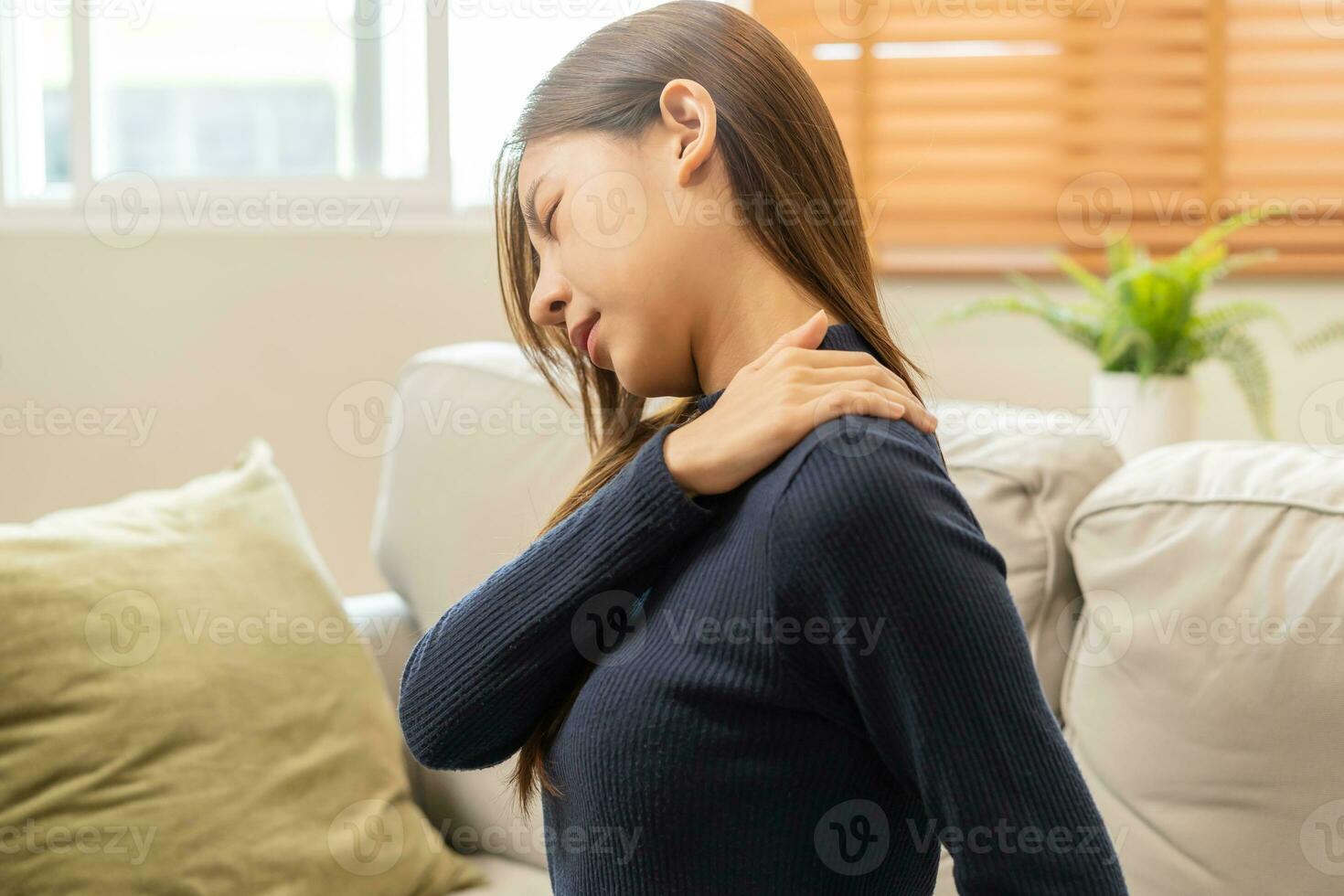 Body muscles stiff problem, asian young attractive woman, girl pain with back pain ache from work, holding massaging rubbing shoulder hurt or sore, painful sitting on sofa at home. Healthcare people. photo