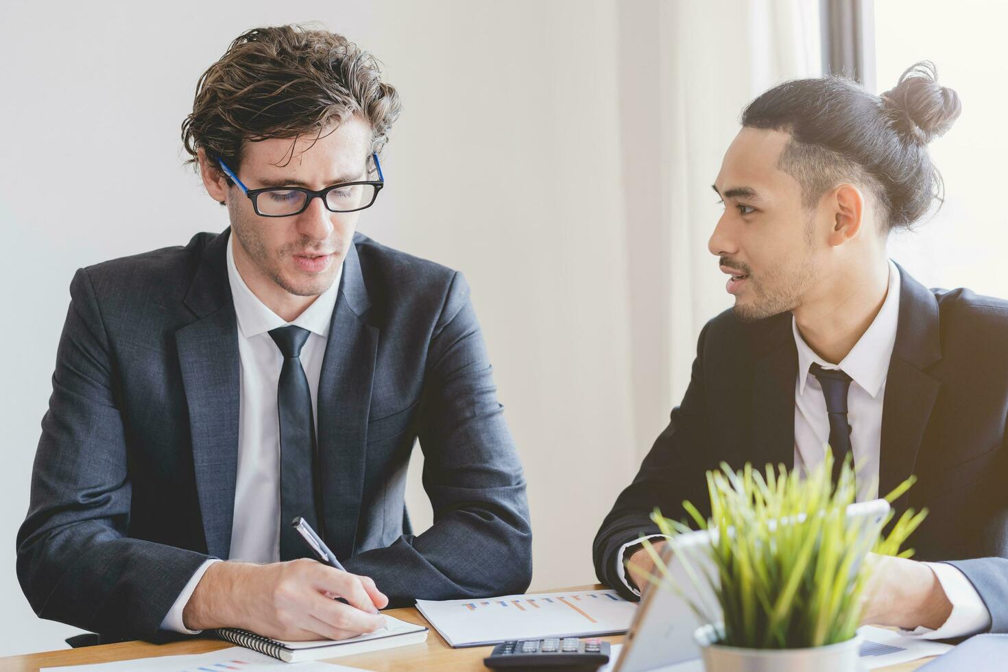 Business meeting, two caucasian, asian group man use tablet brainstorm analyzing on graph data of cost plan or document, paperwork and discussing in board room on table. People working conference room photo