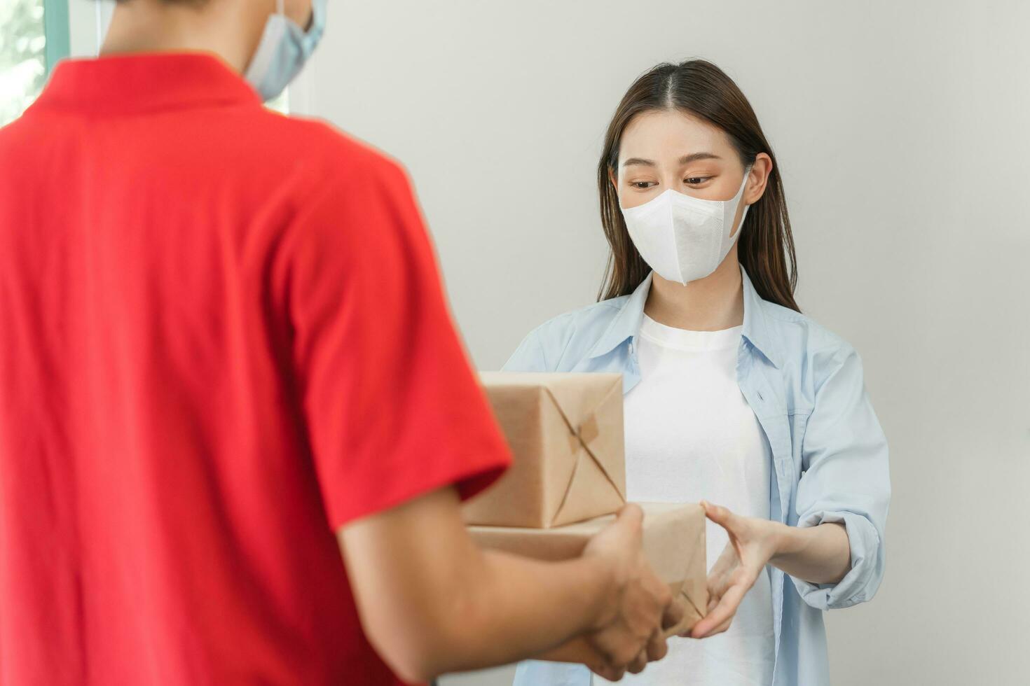 asiático joven mujer, cliente recibido un entrega de cartulina caja, paquete o empaquetar desde entrega, cartero, vistiendo cara máscara debido a aislamiento, cuarentena de covid-19 a el puerta, Entrada de su hogar, casa. foto