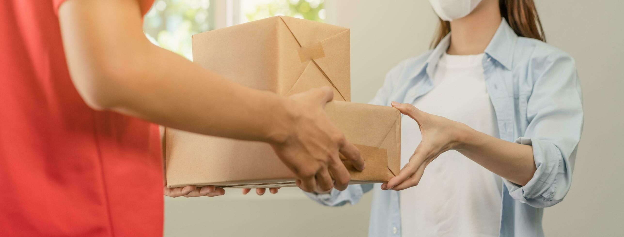 entrega, asiático joven hombre, masculino cartero participación cartulina caja parcela, caja de cartón o correo en rojo uniforme enviar a cliente, cliente mujer recibido desde Mensajero, Servicio negocio, compras en línea. foto