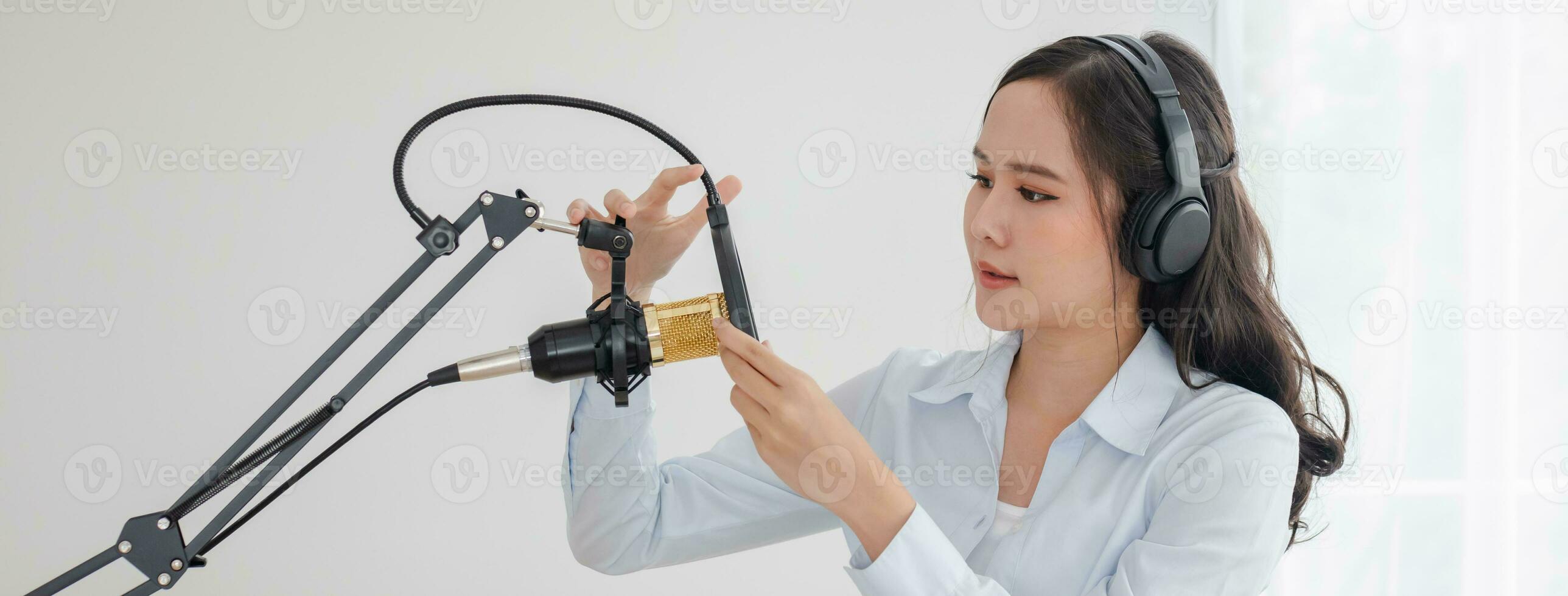 Beautiful asian young woman radio host working, setting microphone, preparing to speak before recording podcast and live on social media. Technology of on-air online in broadcasting at home studio. photo