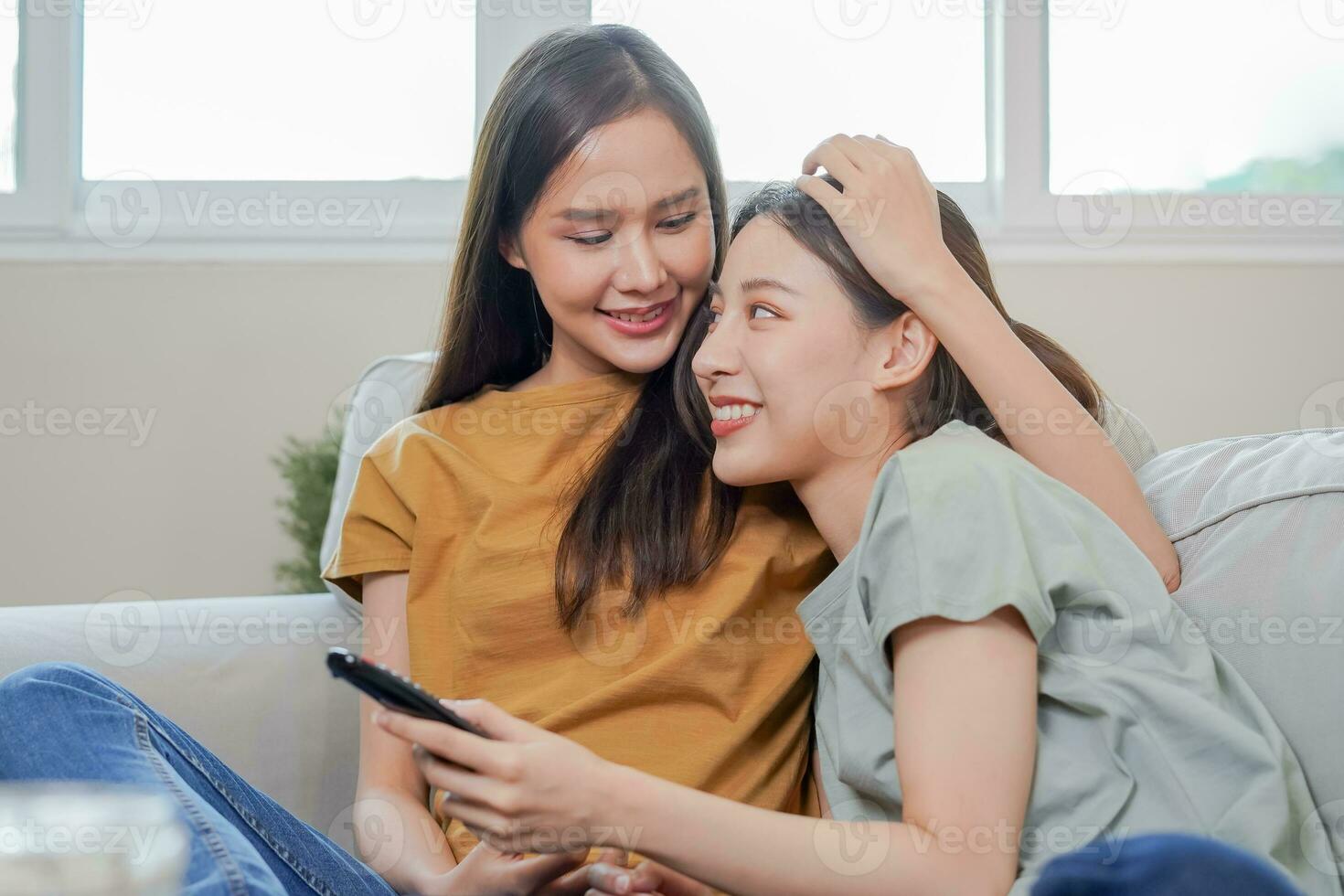 Happy lesbian, pleasure asian young two women, girl gay or close friend, couple love using remote control watching TV, moment spending good time together on sofa at home. Activity of leisure, relax. photo