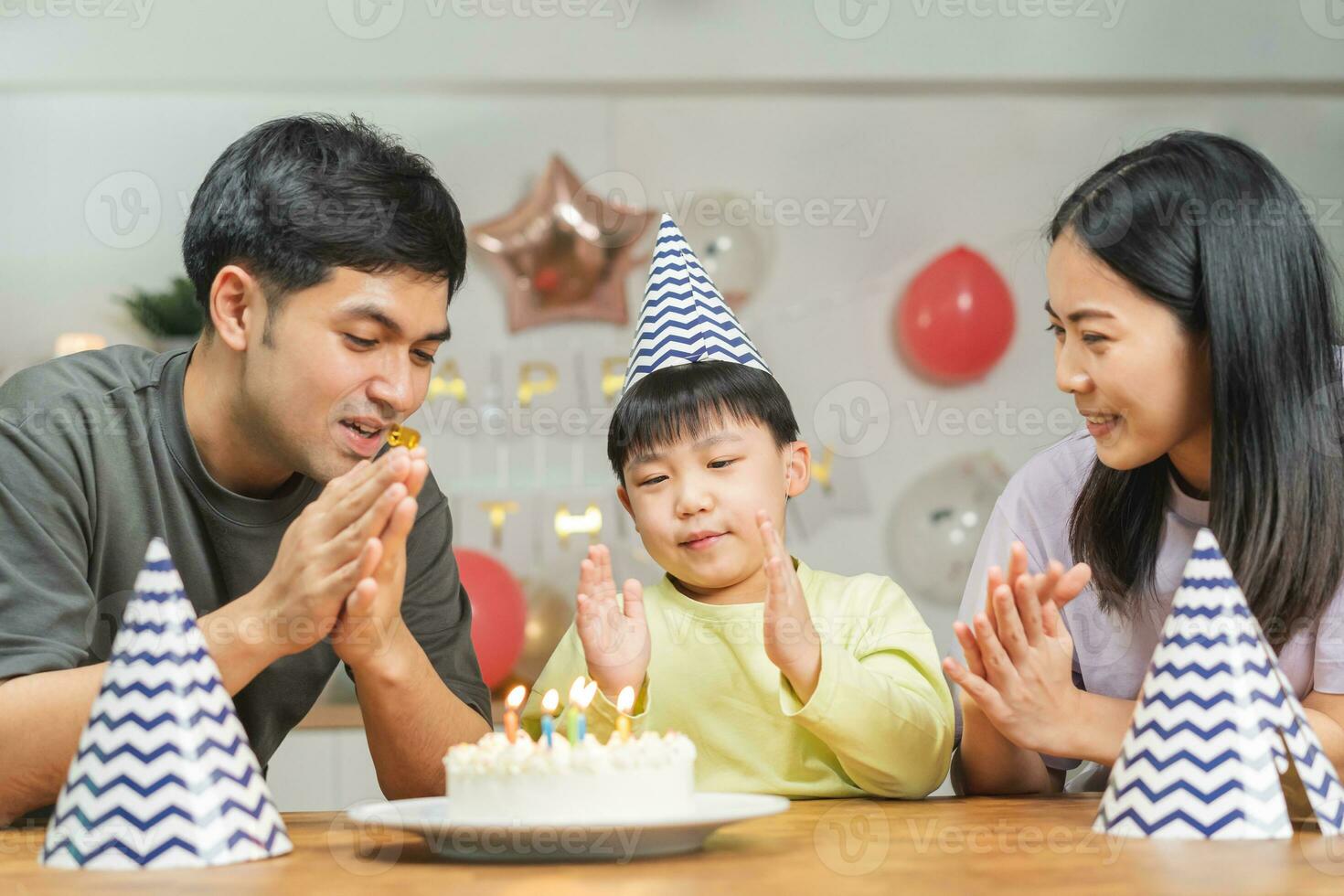 Happy birthday party in family, asian young parent father, mother and little cute boy or child celebrating, blowing candles on the cake and decorated balloons, celebration at home. Lovely moments photo